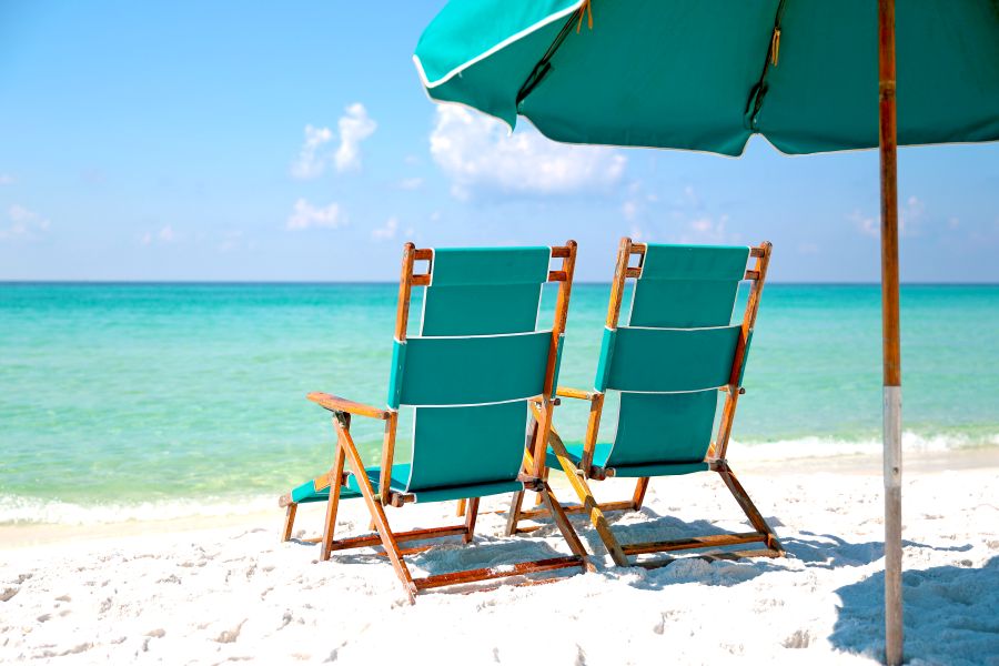 Two beach chairs and an umbrella on the sand facing the water