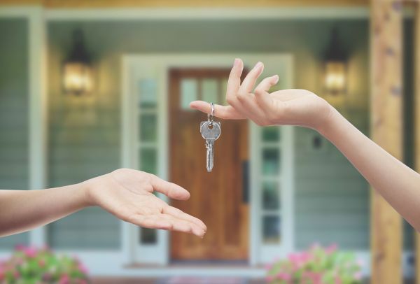 Buying or building a home A hand hanging keys off to another hand in front of a house